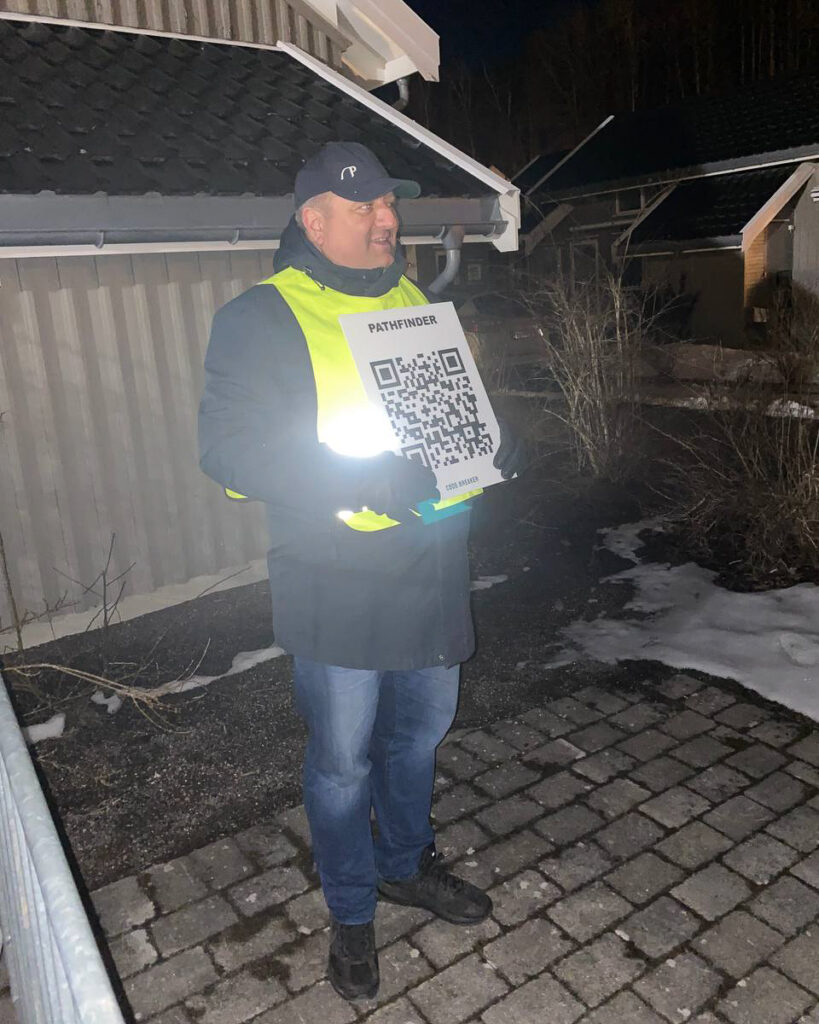 Einar (50) står utendørs på post, med QR-kode som inneholder hint til løsning av oppgaven. Oppgavene er inspirert av Bergpreken-prosjektet ungdommene har jobbet med de siste månedene.